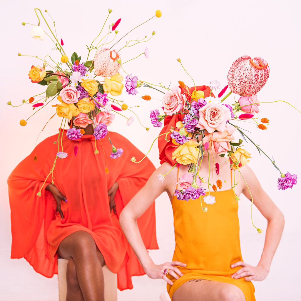 two models seated with tonal dressing and flower bomb bouquets blocking their face. 