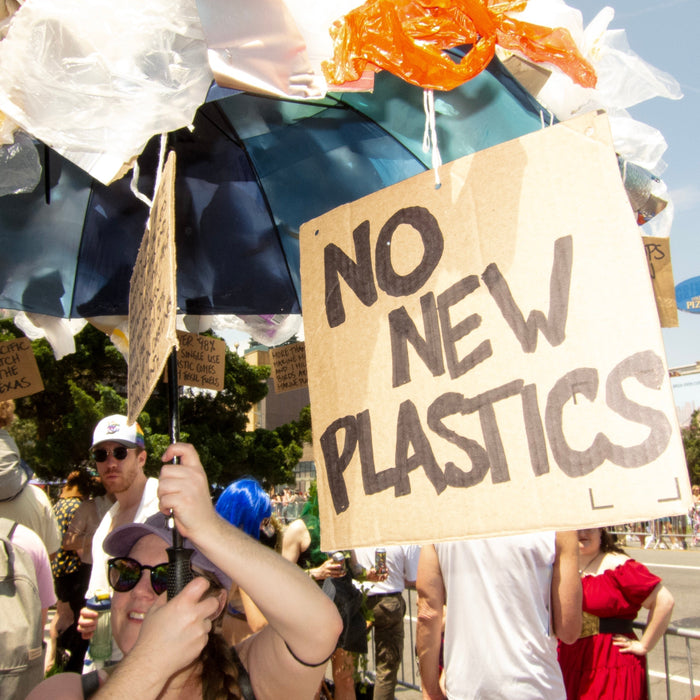 parade goer with protest jellyfish umbrella made of plastic bags - sign hanging reads: no new plastics