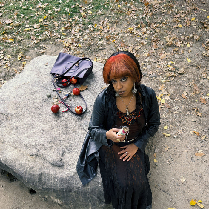 editorial shot of woman sitting on rock with purse full of apples