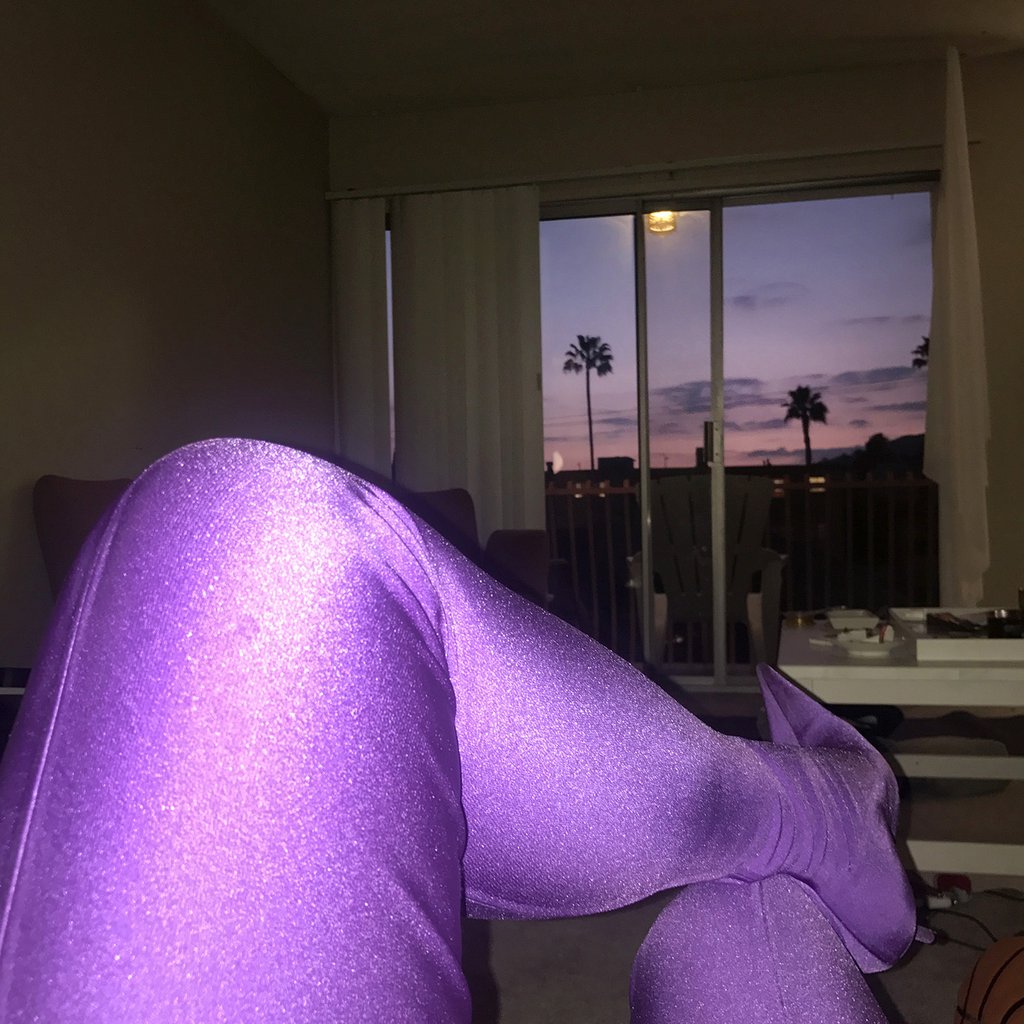 person's legs in purple tights sitting in front of a window and purple sky.