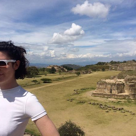 person wearing sunglasses, posing with ancient ruins in the background.
