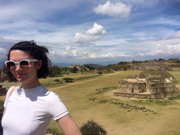 person wearing sunglasses, posing with ancient ruins in the background.