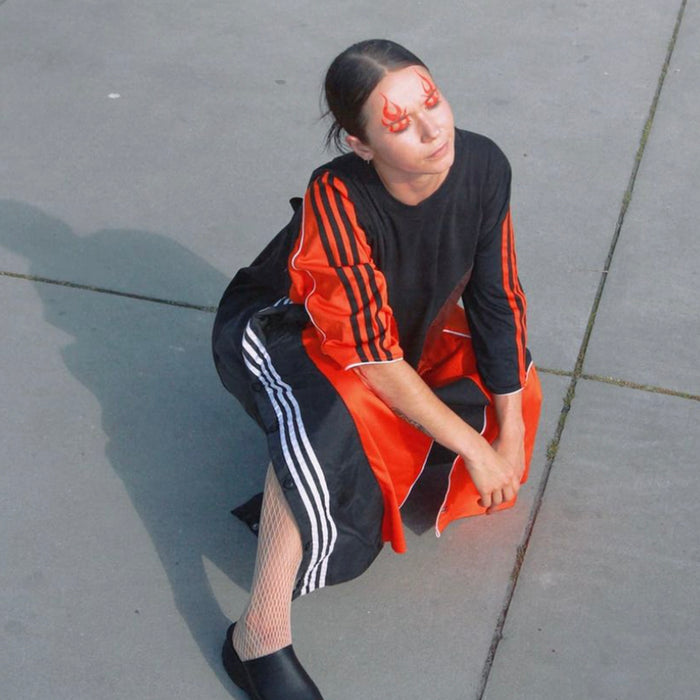 model squatting with up-cycled adidas dress and flame makeup.