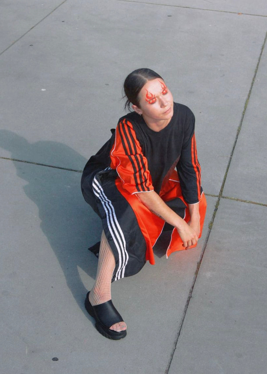 model squatting with up-cycled adidas dress and flame makeup.