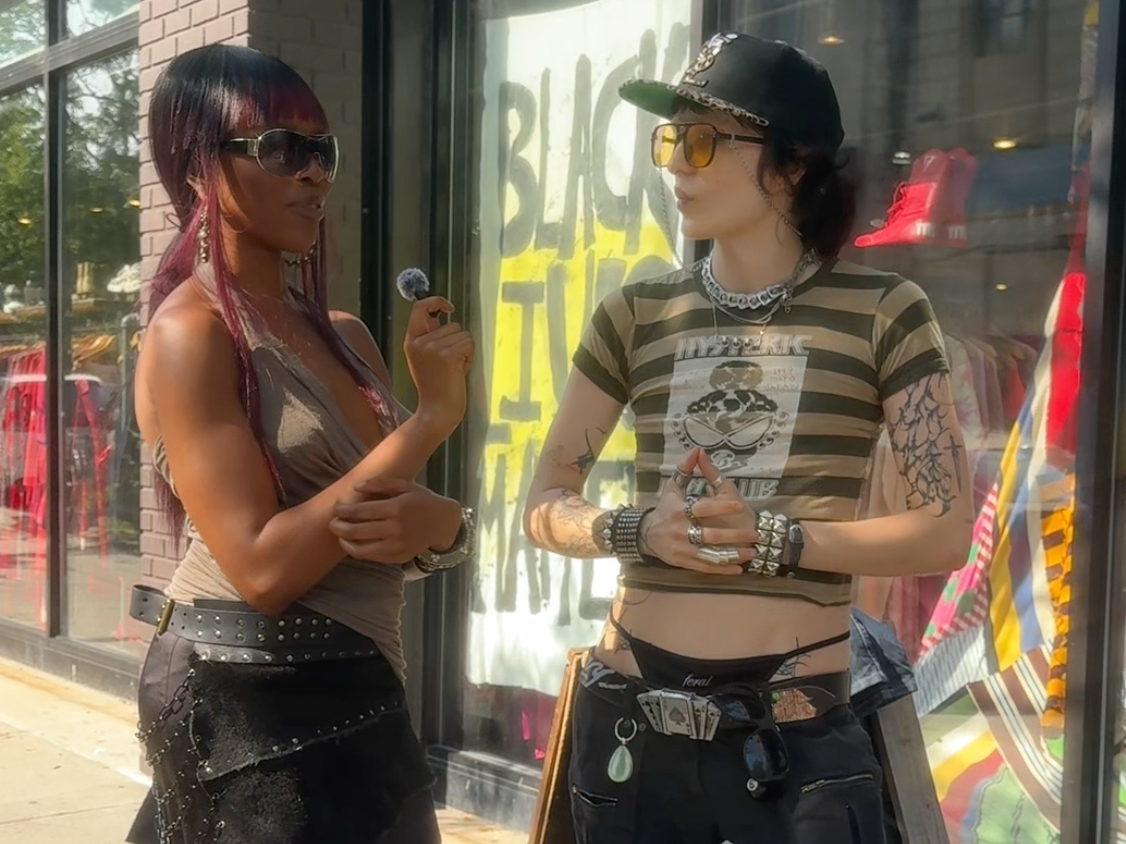 an image of odera and eliza in front of beacons closet store, doing an interview. theres a sign behind them that says "black lives matter"