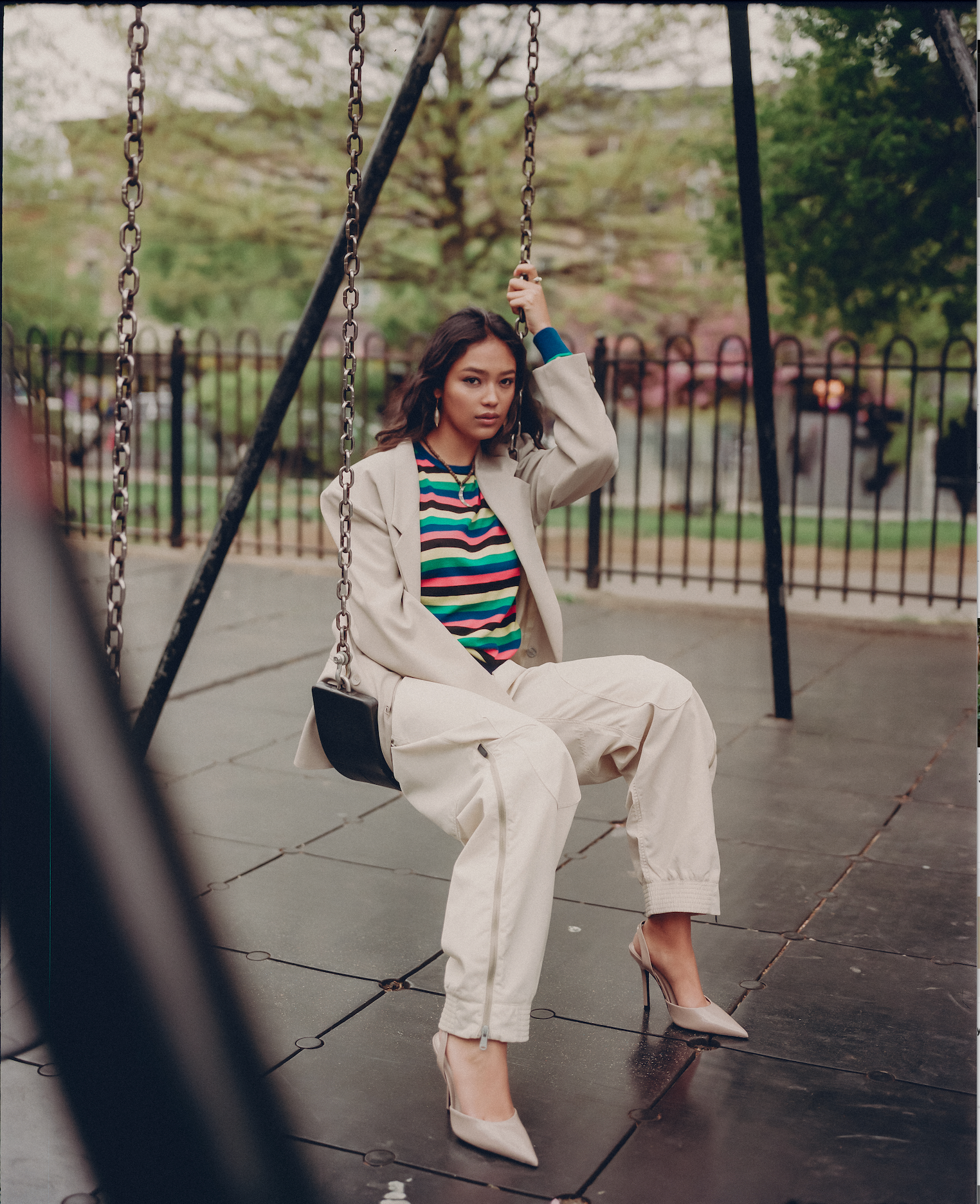 editorial of model in color striped shirt sitting on city park swing set