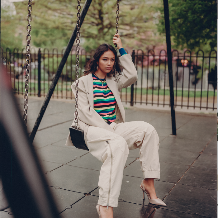 editorial of model in color striped shirt sitting on city park swing set