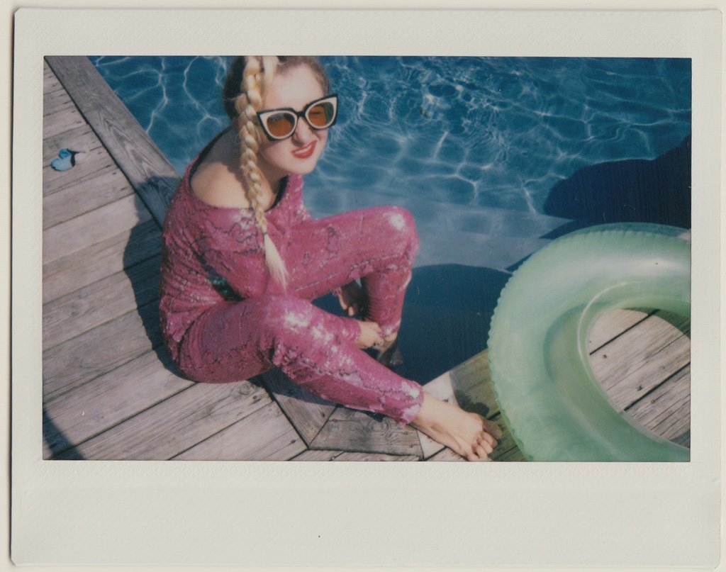 ashley in sequin jumpsuit seated on deck by pool. 