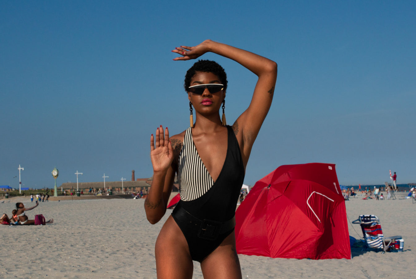 model posing on beach with hand up and one over head. 