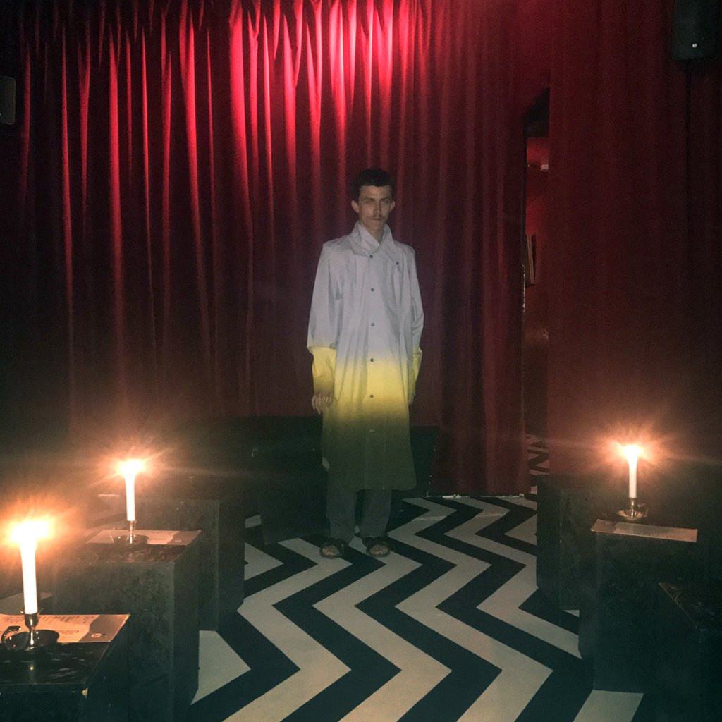 a person standing in a room with candles and red curtain in the background.