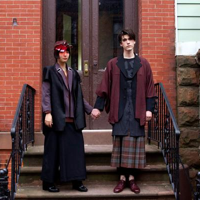 two androgynous models hold hands on a stoop. 