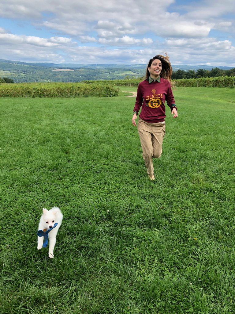 a person running in the fields with a white little dog.