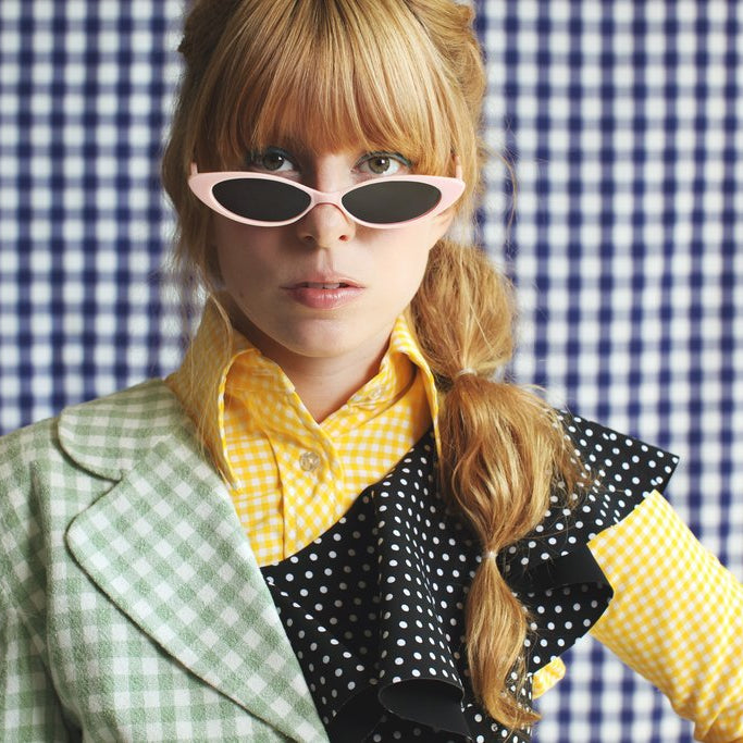model in slim sunglasses mixed check prints and polka dots in front of a checked backdrop .