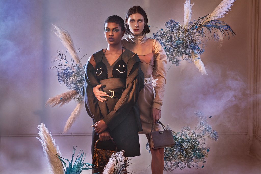 two models featured in suiting with smoke and floral arrangements hanging around them. 