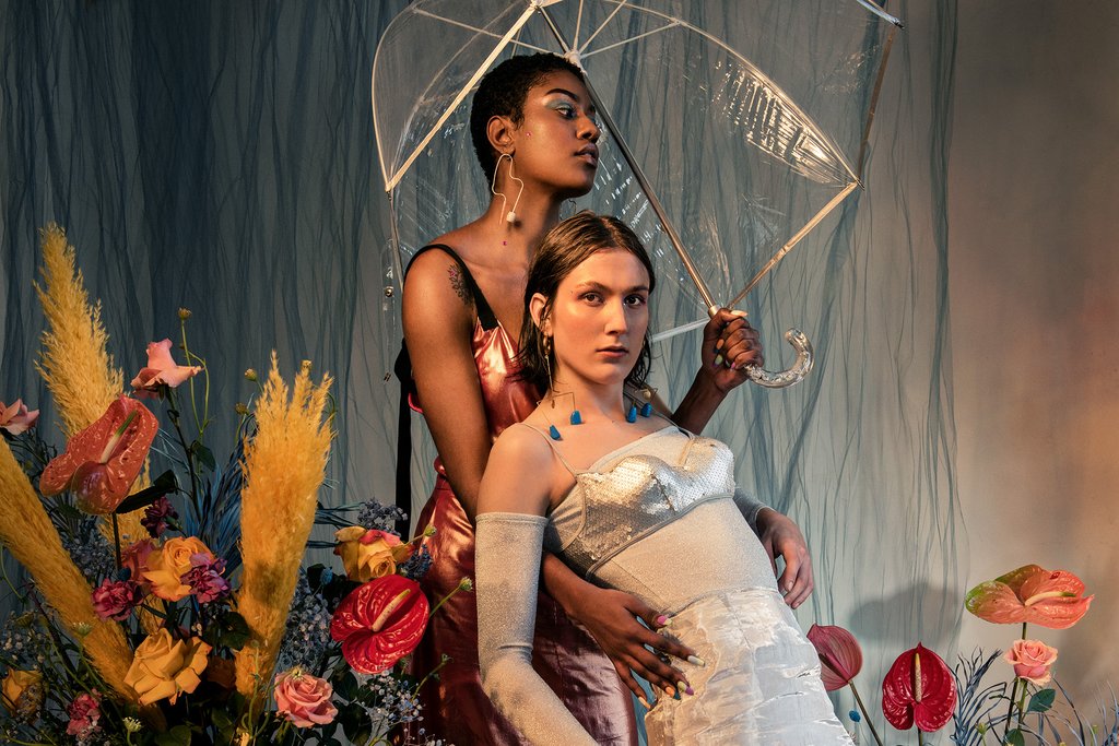 models under clear umbrella with sheer curtain backdrop and floral arrangements.