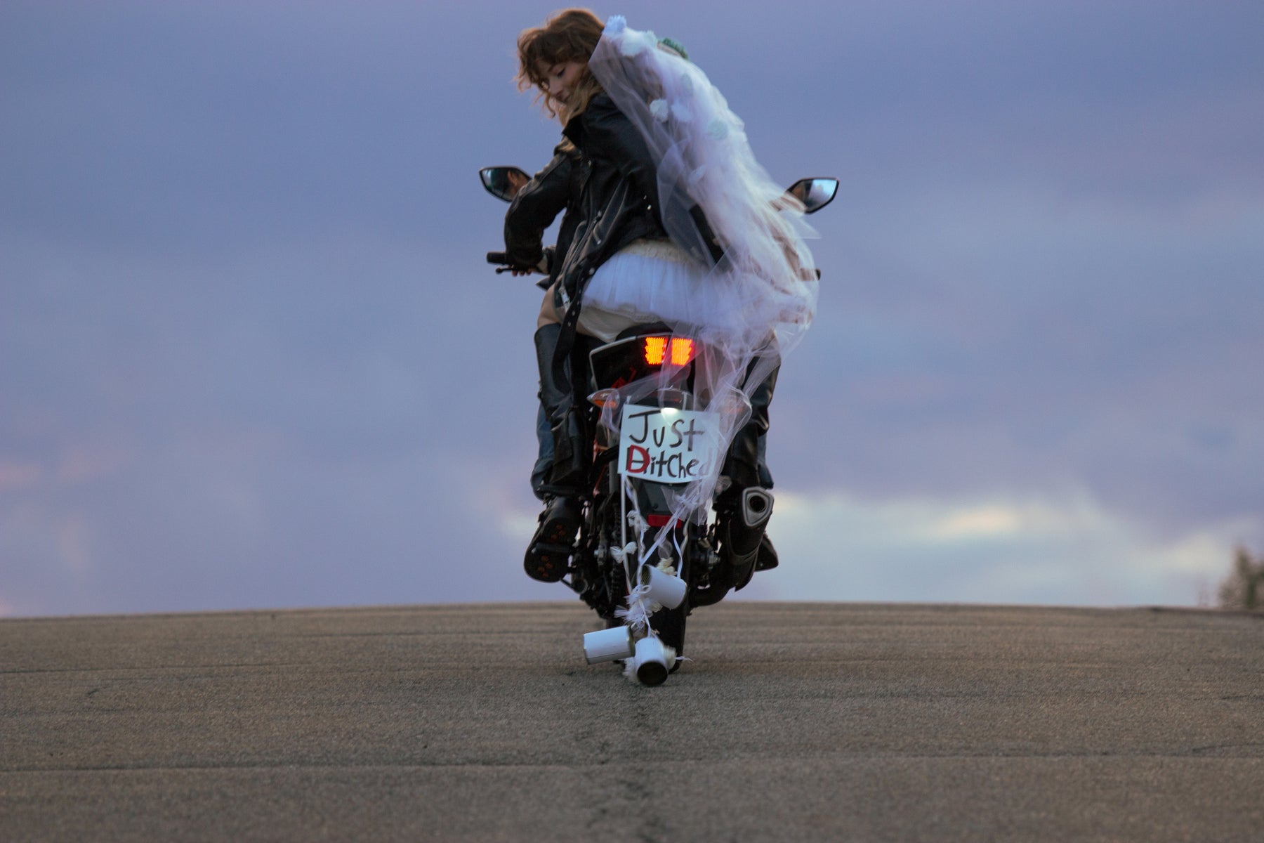 bride riding away on the back of motorbike. sign tacked to back of bike reads: "just ditched".