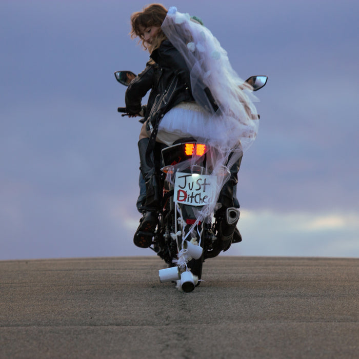 bride riding away on the back of motorbike. sign tacked to back of bike reads: "just ditched".