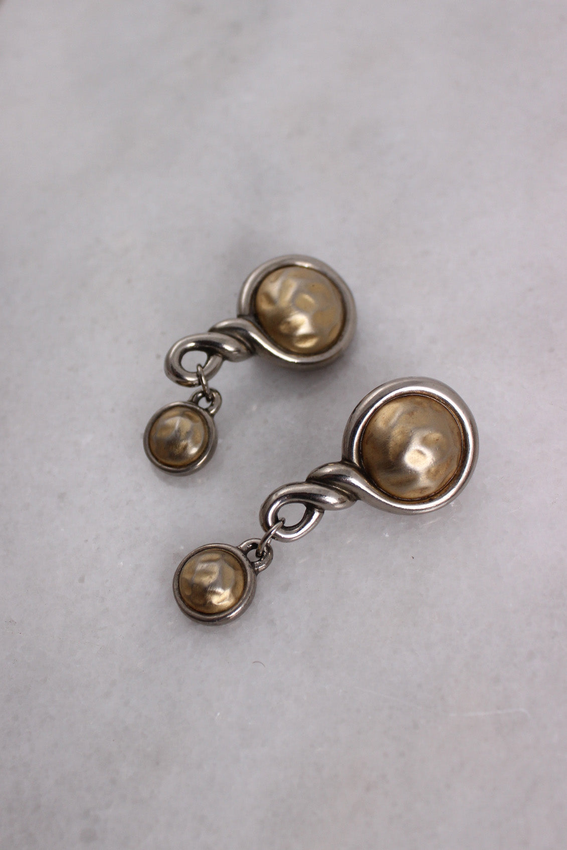 ¾ top view of metallic earrings highlighting hammed rounded center details