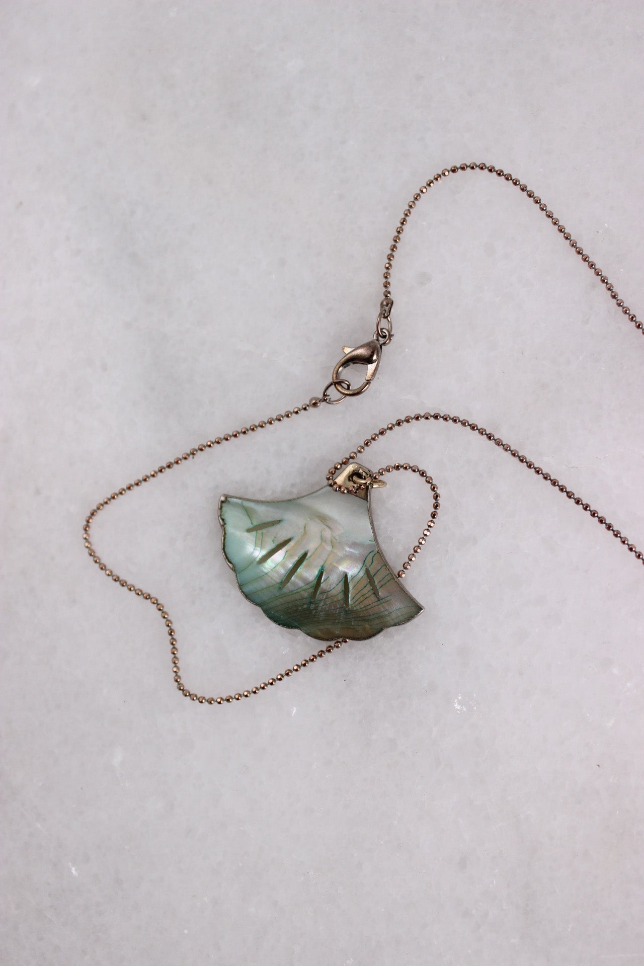 top view of necklace laid flat showcasing lobster claw style closure and opalescent shell-shaped pendant. 
