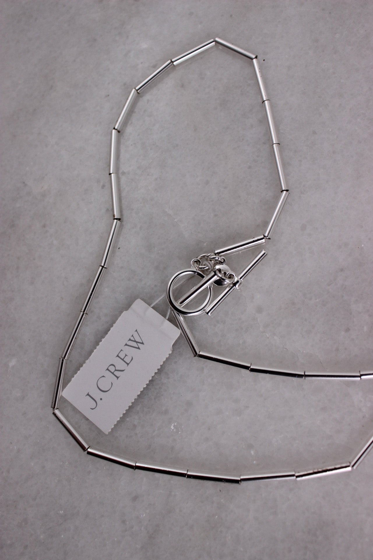 elevated back angle j.crew silver toned metal necklace featuring toggle closure laid on marble background.
