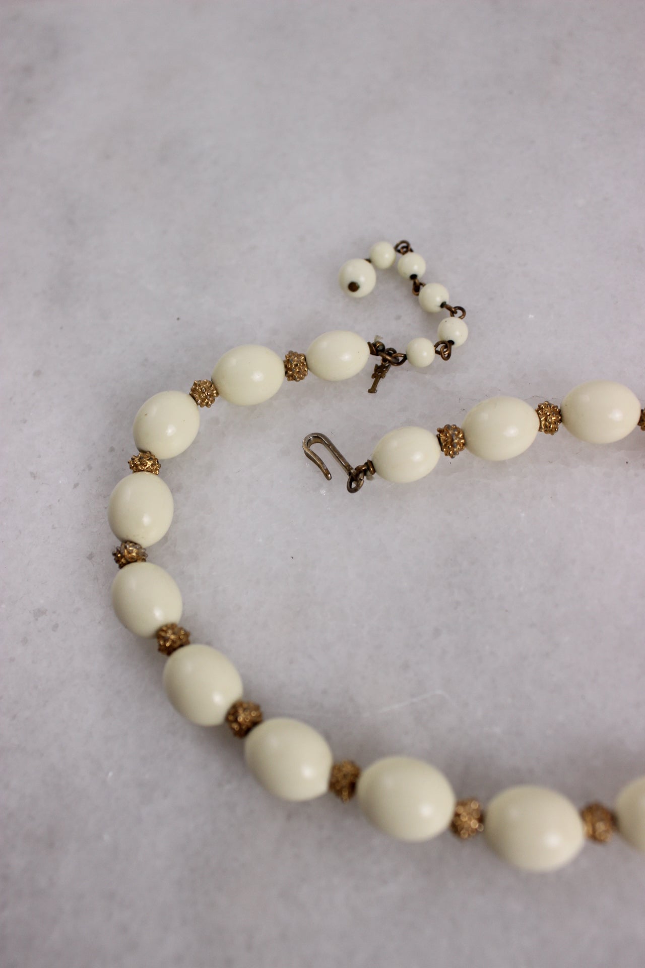 detail of necklace featuring white oval and gold toned beads.