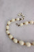 detail of necklace featuring white oval and gold toned beads.