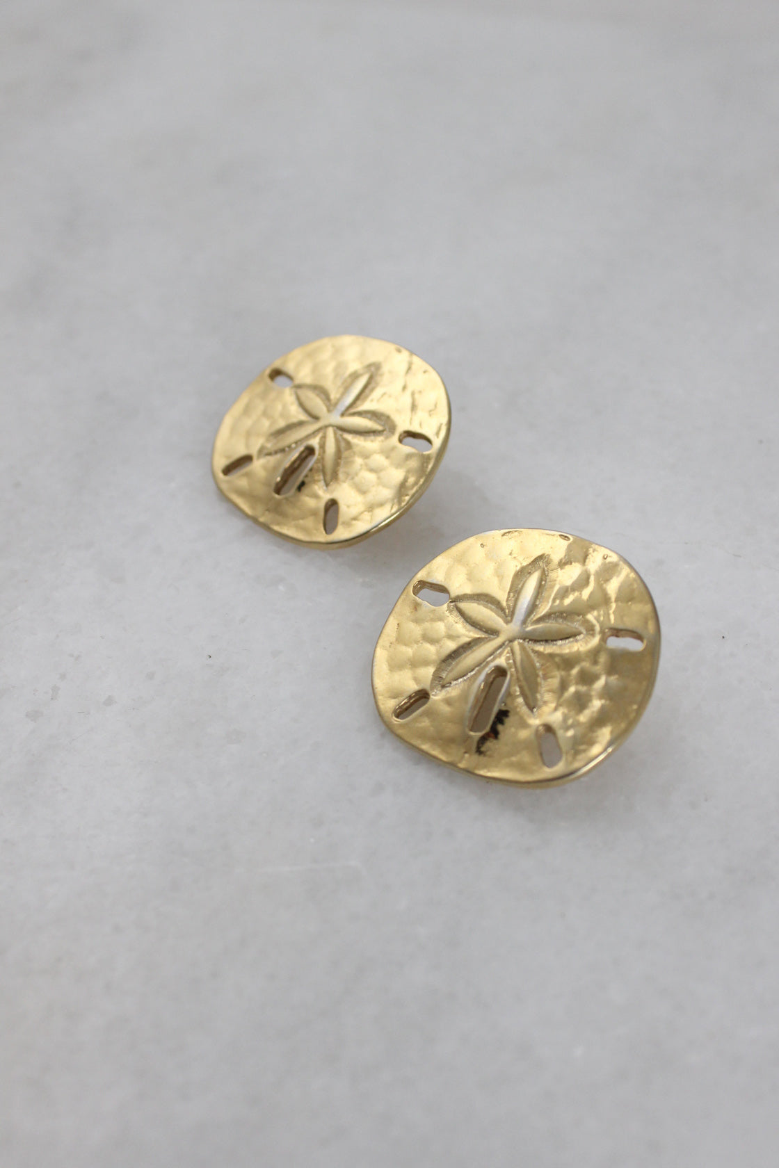  ¾ top view of golden earrings highlighting hammered face with sand dollar-like detailing