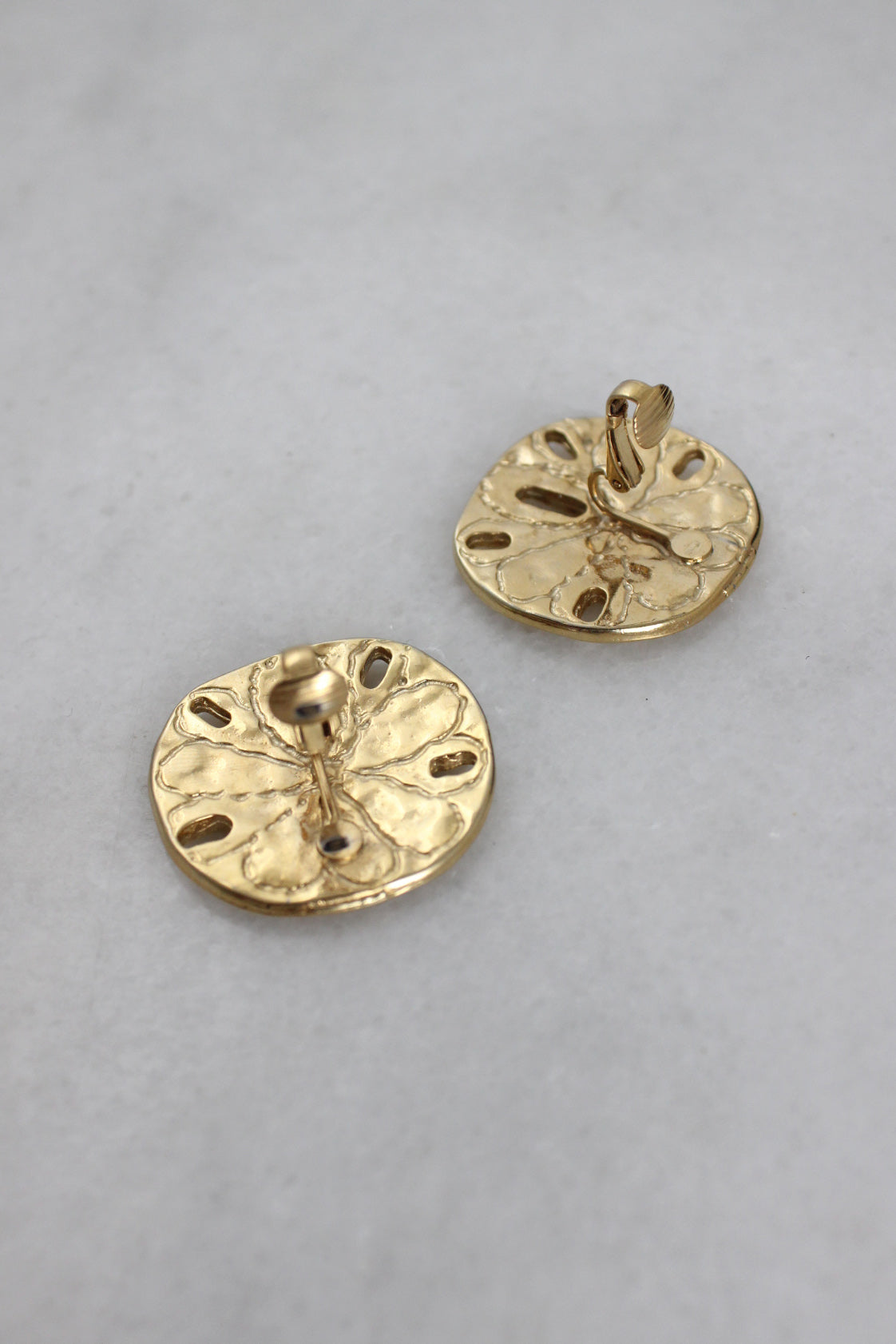 ¾ top view of the back of rounded clip-on earrings showcasing hinge style backs. 