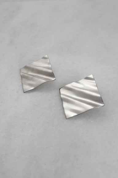 ¾ top view of silver earrings with wavy rippled effect.