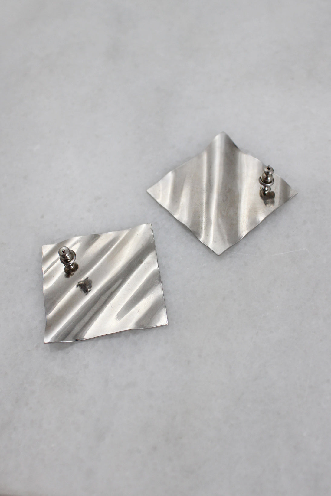 ¾ back of silver rippled earrings with push style backs laid flat.