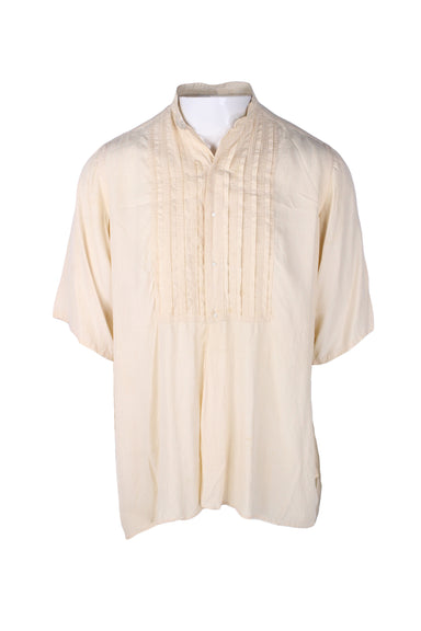 front angle of vintage w.a. mclaughlin 1910 cream button up shirt on masc mannequin. features pleated bib, small button closure up center which ends at mid section, small standing collar, and short sleeves. 