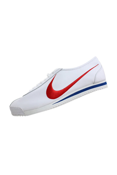 side angle of nike white classic slim sneaker. features red embroidered swoosh on side walls, white leather upper/swoosh on inner wall, flat lace closure, and foam sole with blue stripe.