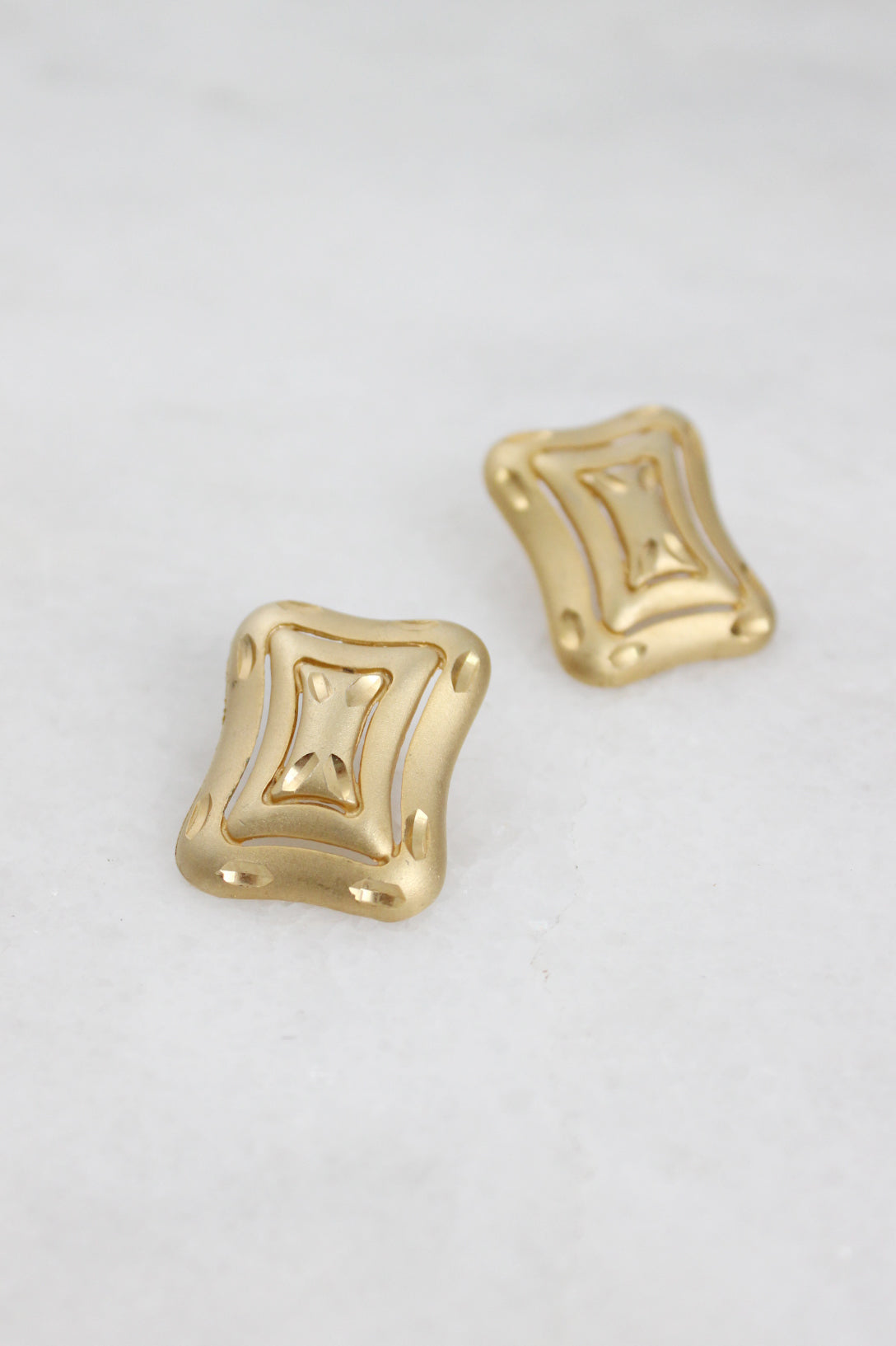 angled top view of rounded, rectangular earrings highlighted carved detailing laid flat.