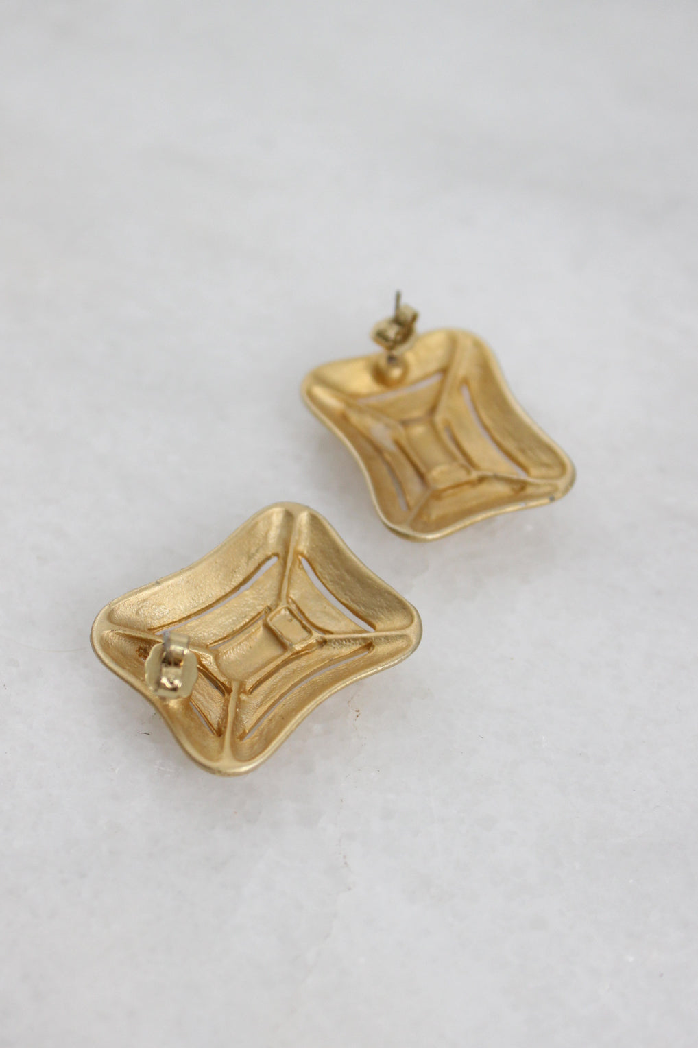 rear of gold toned metallic earrings with butterfly style backs laid flat upside down. 
