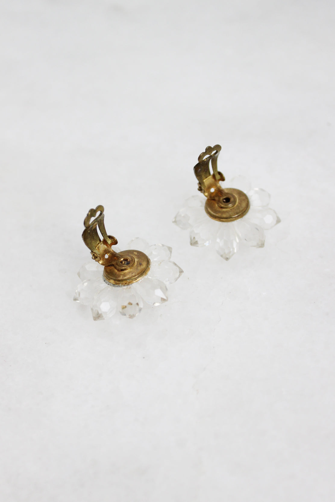 top angle of clear floral earrings staged facing down showcasing aged gold toned hinge-style backs.