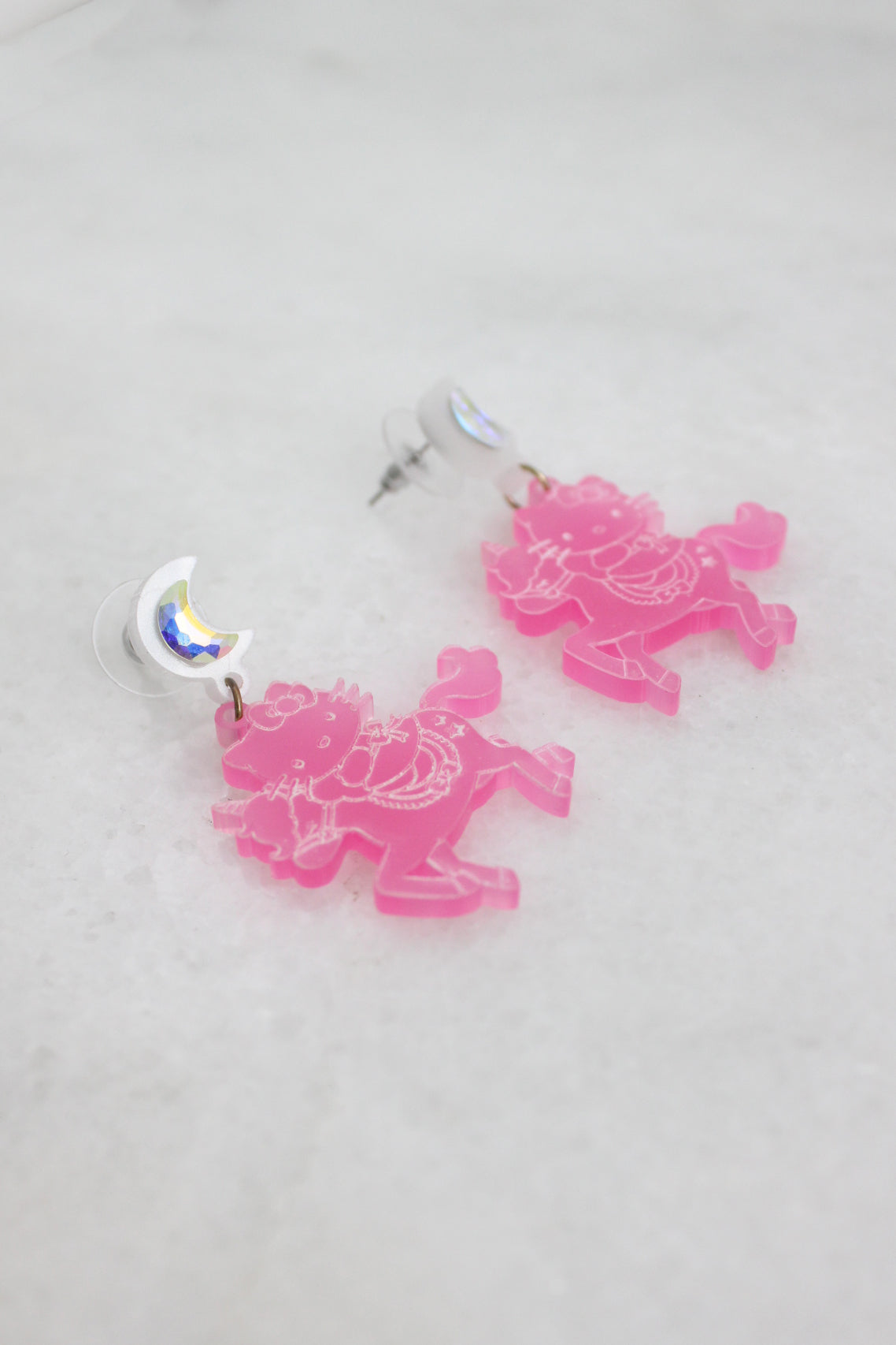 ¾ angled top view of pink earrings with a frost moon-shaped stud adorned with a rainbow effect rhinestone. 
