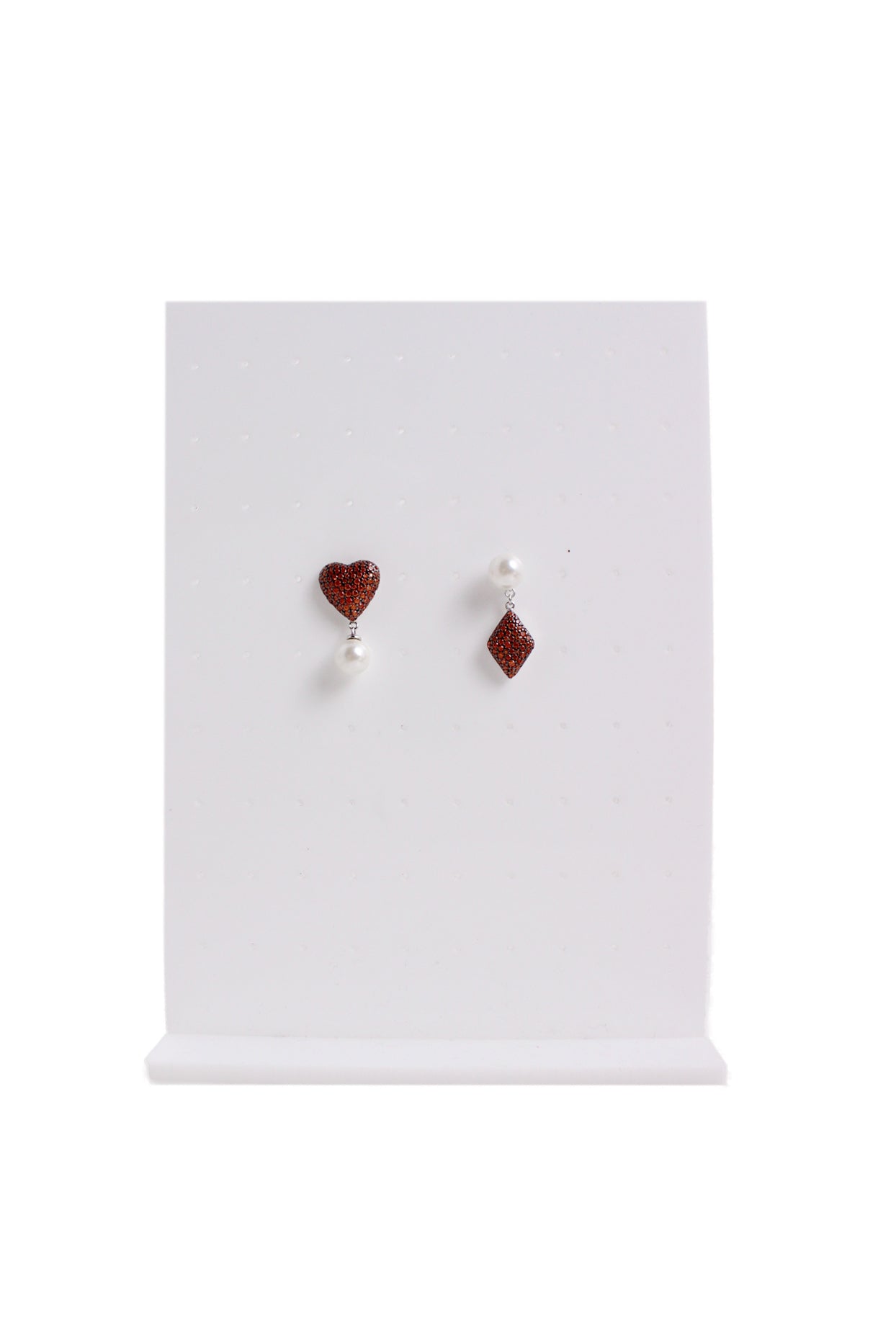orange stoned heart and diamond shaped earrings with white pearl bead staged on an earrings stand. 
