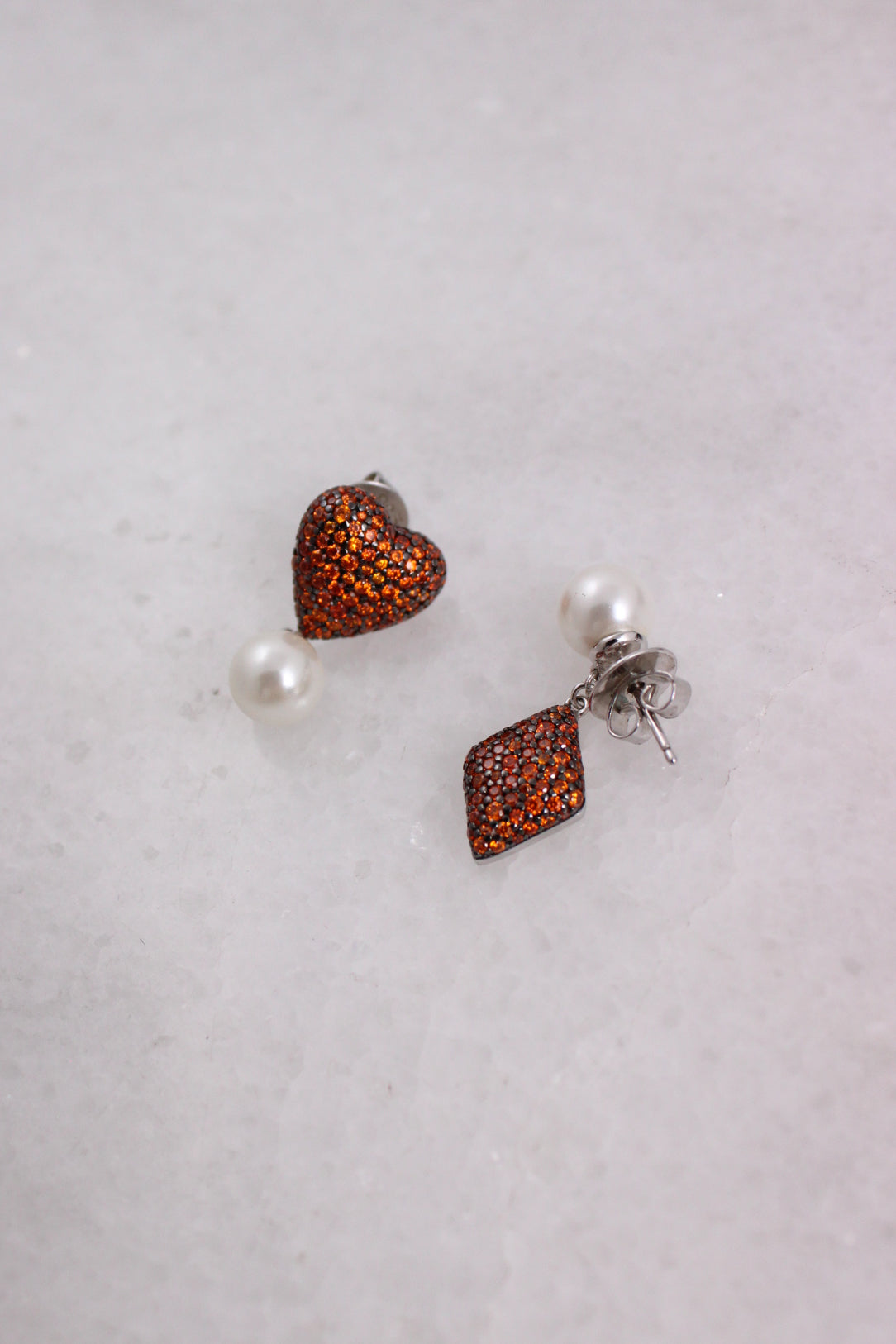 ¾ angle top detailed view of heart and diamond chapped earring charms adorned with orange ministones laid flat.