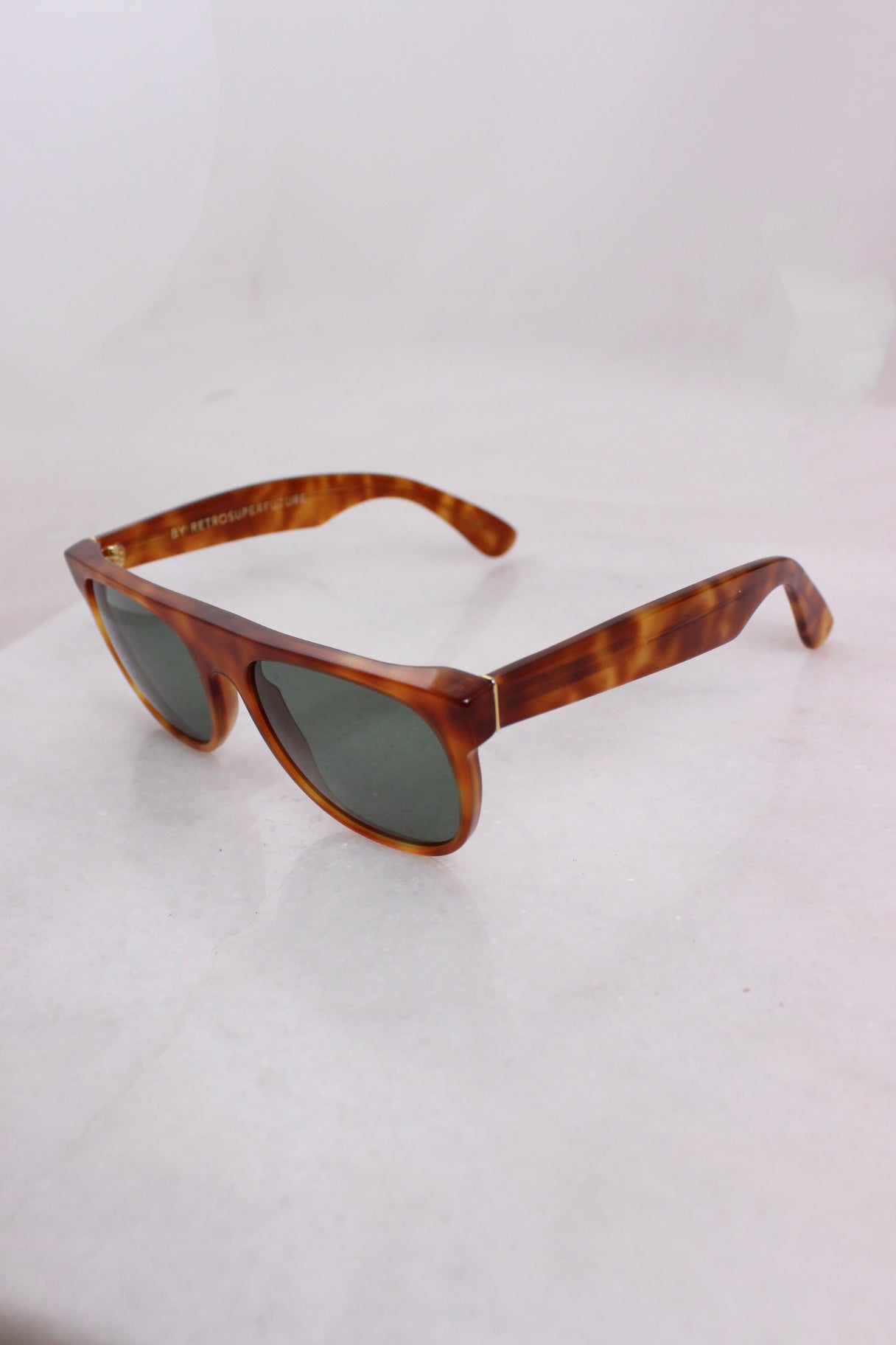 ¾ angled top profile of brown toned sunglasses with black tinted lenses and metallic gold toned hardware