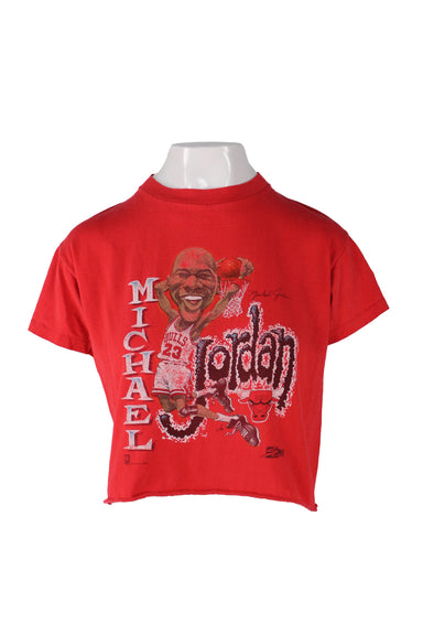front angle of vintage red michael jordan bulls t-shirt on fem mannequin. features cartoon figure of jordan dunking a ball behind his head, stylized text with name 'michael jordan', bulls logo, brand with date 1990, cut off hem, high rounded ribbed collar, and short sleeves with single stitch hem. 