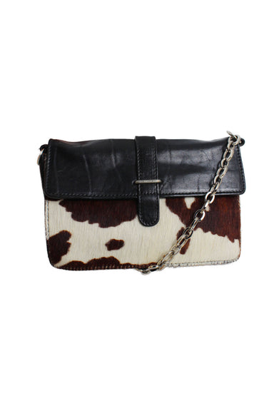 front of furla black leather flap top hand bag. features cow fur at front, rectangular shape, embossed brand at silver tone hardware, silver metal chain, and snap button closure.  