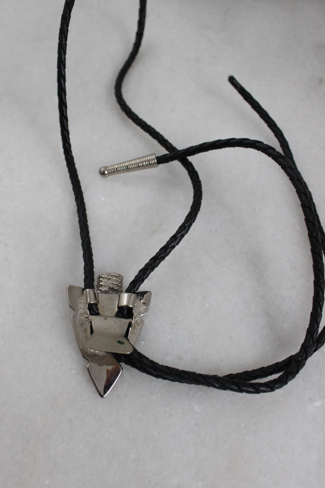 rear of bolo tie laid flat showcasing the arrowhead shaped centerpiece’s hinged back 