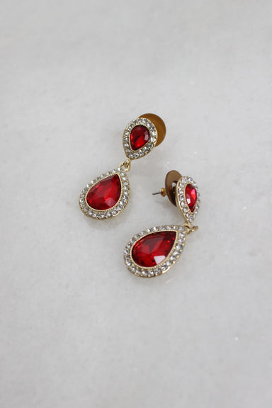 angled top view of earrings laid flat showing the red cut stone studs framed by miniature white stones.