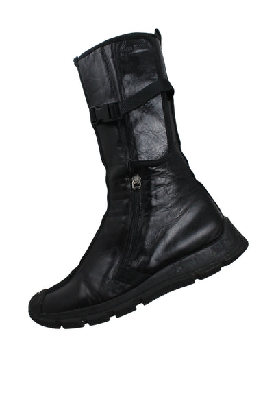 profile of vintage miu miu archival black leather future combat boots. 10.5" tall boot shaft, with side zipper, velcro flap, and nylon belted calf strap closure. rubber soles. signs of wear at bottom of soles, sold in "as is" condition (see photos). mesh netting lining. 