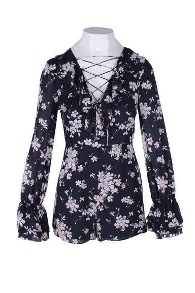 front of intermix blue navy long sleeve overall. features floral print throughout, v neckline with interlaced drawstring, ruffled design at neck/cuffs, elasticized at cuffs, and above-knee length.