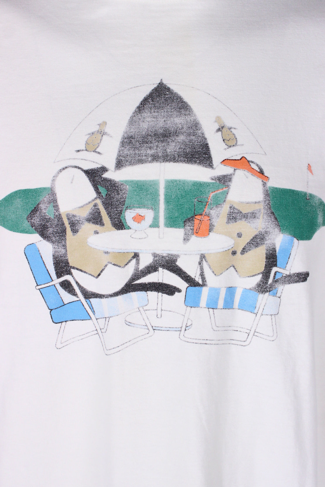 detail of print of two penguins lounging in lawn chairs at golf course. one is drinking out of a straw and the other has a goldfish in a glass. 