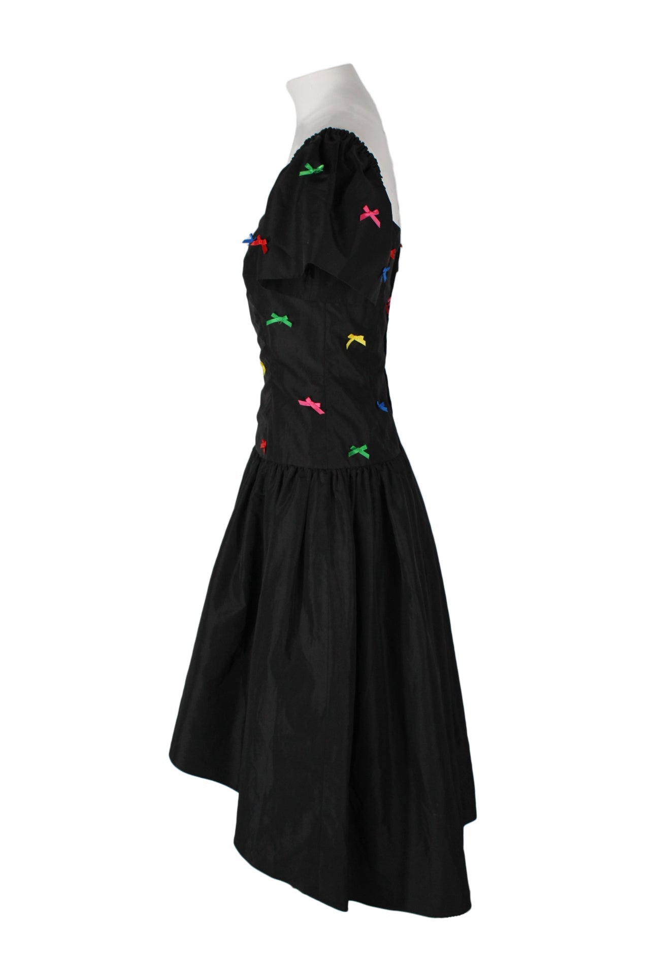 side angle of vintage party dress on feminine mannequin featuring multicolor bow embellishment at upper, dropped waist, and high-low hem.