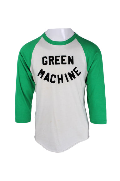 front angle of vintage green and white three-quarter sleeve t-shirt on masc mannequin torso. features green raglan sleeve, press on black text 'green machine' across chest, rounded rolled hem, and care tag dates shirt to the 1980's. 