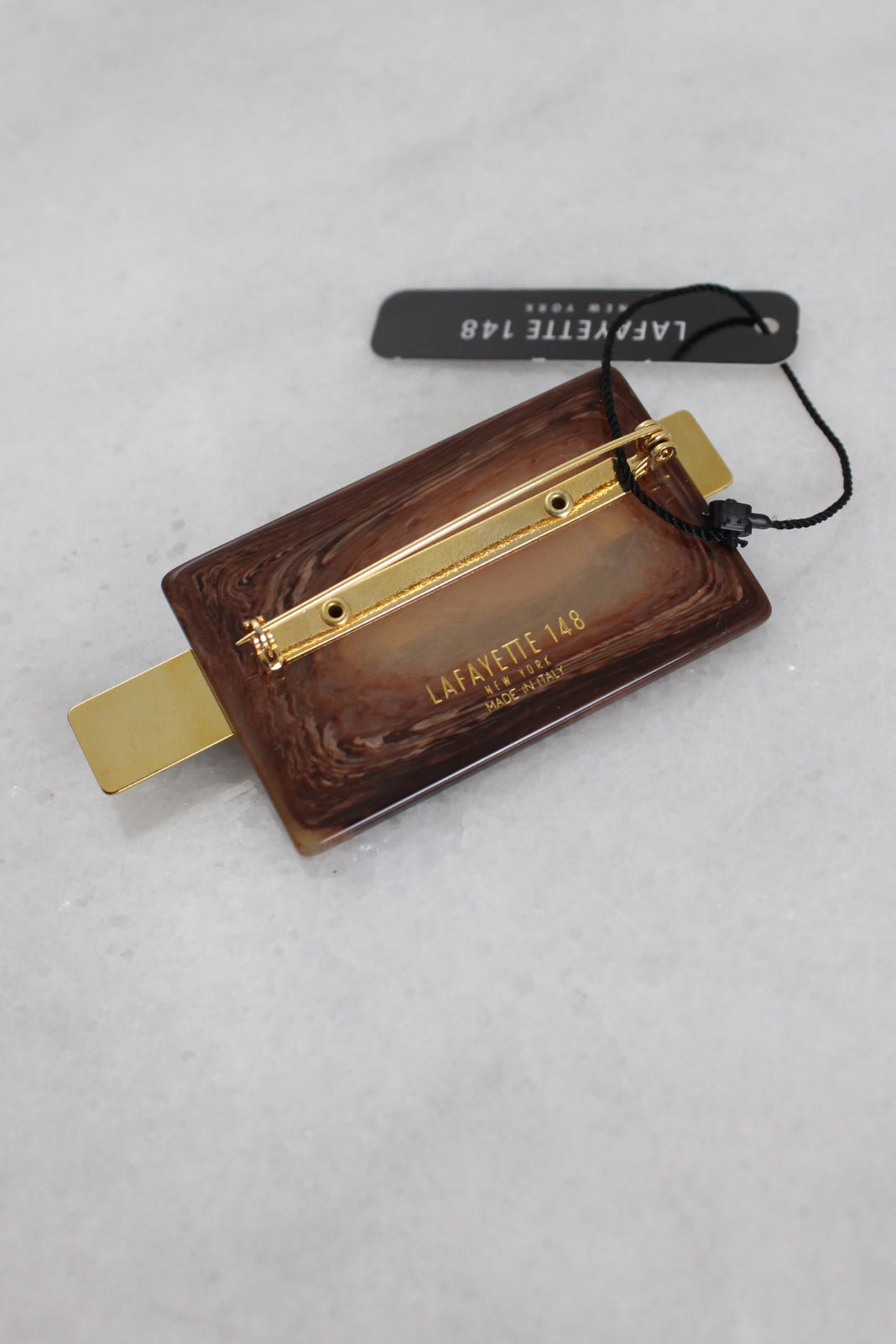 ¾ angled back view of brown brooch with gold toned metallic pin back and brand engraving.