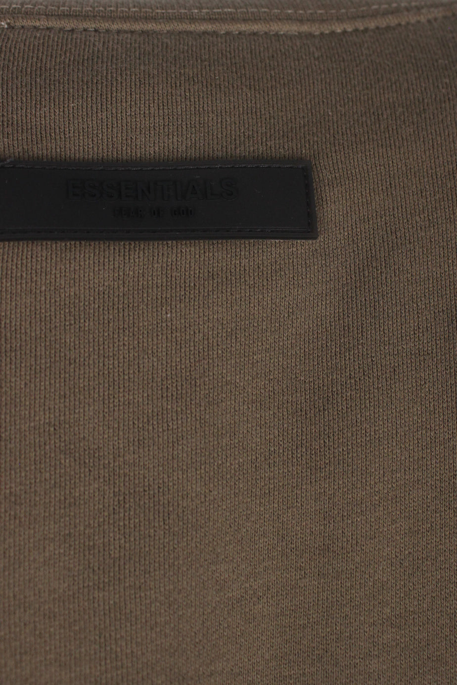 detail view of rubber 'essentials fear of god' logo tag at back of sweatshirt.